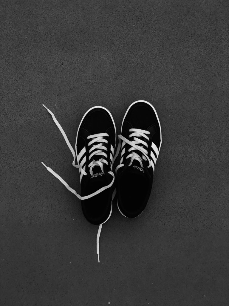 A close-up shot of black sneakers with white laces on a dark surface.