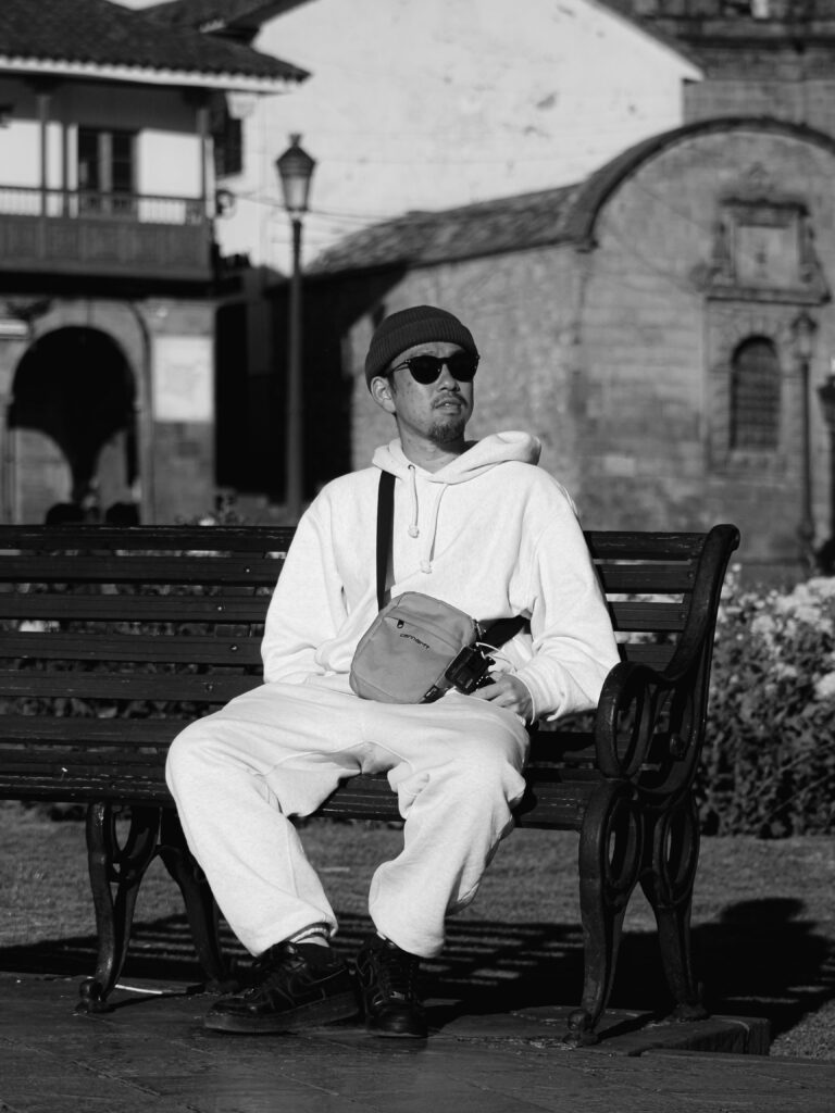 A man sits on a bench in Cusco, Peru, reflecting local architecture and a peaceful atmosphere.