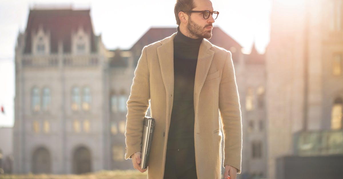 Fashionable young man with a laptop walking in the sunlight near a historic building in Budapest.